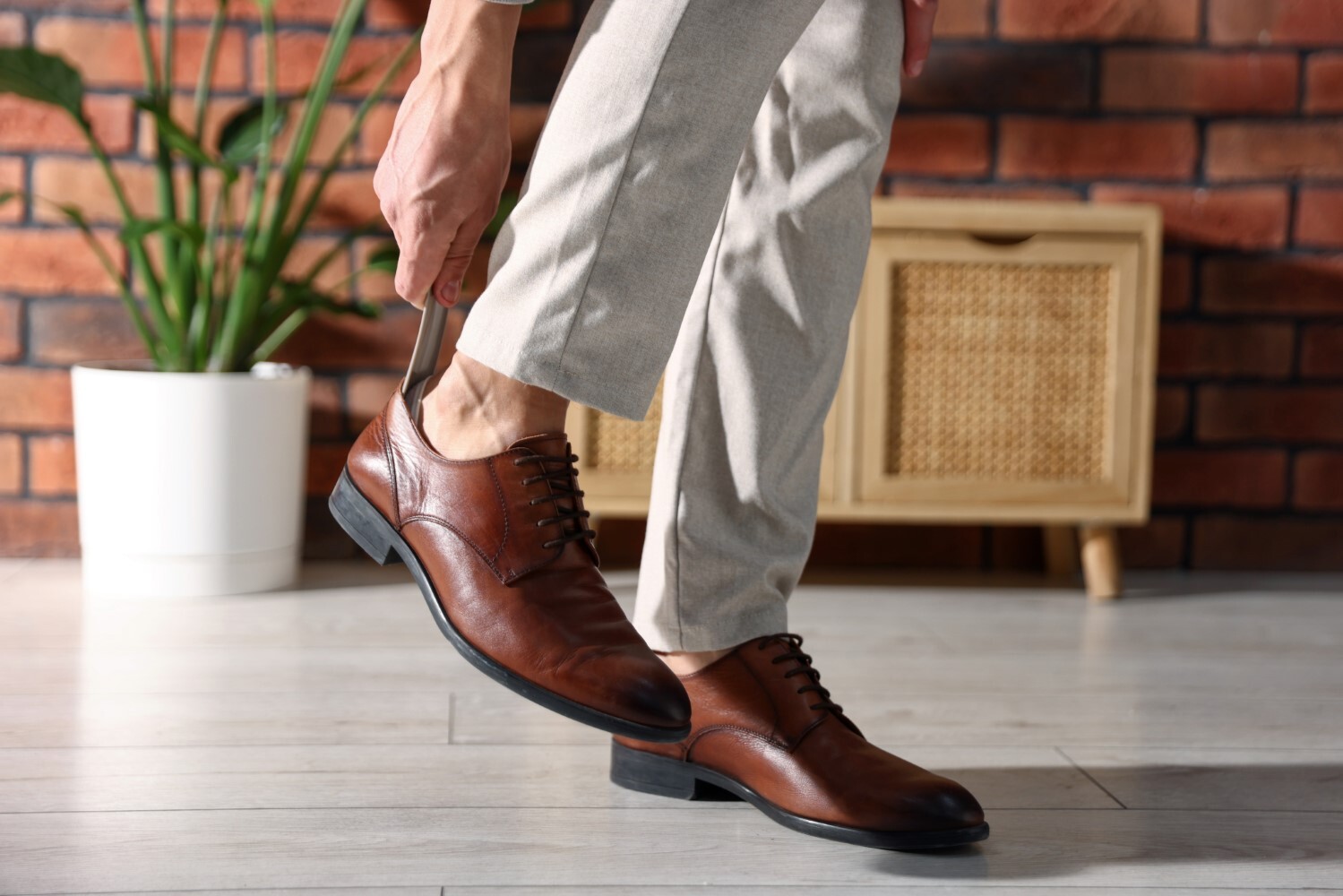 Man putting on stylish shoes with shoehorn indoors, closeup